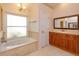 Bright bathroom featuring a marble-trimmed tub, elegant gold-framed mirror, and warm wood vanity at 9681 Lake Douglas Pl, Orlando, FL 32817