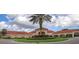 Clubhouse entry features a tall palm tree in the roundabout, red tiled roofs, and lush landscaping at 3661 Kingswood Ct, Clermont, FL 34711