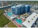 An aerial view of a blue apartment building with two pools, patios with lounge chairs, and surrounding neighborhood at 611 S Atlantic Ave # 4212, New Smyrna Beach, FL 32169
