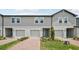 Gray two-story townhome featuring individual garages, neatly trimmed landscaping, and a blue front door at 16466 Bird Of Paradise Ave, Clermont, FL 34714