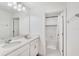 Bright bathroom with double sinks, white cabinetry, and a doorway leading to a shower with a tiled accent wall at 2680 Nottel Dr, St Cloud, FL 34772
