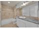 Bright bathroom featuring travertine tile, granite countertop, bathtub and shower combination, and a large mirror at 312 Grand Bay Ln, Celebration, FL 34747