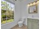Bright bathroom features a tiled floor, toilet, vanity, decorative mirror, and window with a view of outside greenery at 312 Grand Bay Ln, Celebration, FL 34747