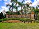 Welcoming community entrance featuring an elegant stone sign, colorful landscaping, and mature palm trees for an inviting arrival at 5062 Otters Den Trl, Sanford, FL 32771