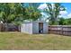 An open gray shed sits on a grassy lawn, enclosed by a wooden fence, adding extra storage in the backyard at 2811 Citron Dr, Longwood, FL 32779