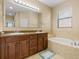 Bathroom featuring double vanity, large mirror, soaking tub with beige tile surround at 1023 Hermosa Way, Kissimmee, FL 34744