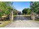 View of a house and yard beyond the stone and wood entry posts and a black metal driveway gate at 21343 Reindeer Rd, Christmas, FL 32709