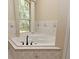 Bright bathroom featuring a tiled corner soaking tub beneath a large window with leafy green tree views at 3441 Hickory Creek Rd, Deltona, FL 32738