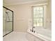 Bright bathroom features a glass shower and a tiled corner soaking tub beneath a large window with leafy green tree views at 3441 Hickory Creek Rd, Deltona, FL 32738
