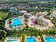 Aerial view showcasing a community pool, splashpad, slides, and many lounge chairs surrounded by lush palm trees at 7643 Wilmington Loop, Kissimmee, FL 34747