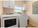 Bright laundry room features modern washer and dryer, storage cabinets, and natural light from window at 240 Spring Forest Dr, New Smyrna Beach, FL 32168