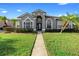 Charming gray home featuring tropical landscaping, arched windows, and a pathway leading to the front door at 9885 Montclair Circle Cir, Apopka, FL 32703