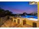 Outdoor kitchen with stainless steel grill with view of an illuminated pool during twilight at 1710 Bridgets Ct, Kissimmee, FL 34744