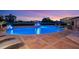 Luxury pool featuring a waterfall at dusk. Pool is surrounded by professional landscaping and outdoor lighting at 1710 Bridgets Ct, Kissimmee, FL 34744