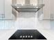 Close-up of a kitchen stovetop with a stainless steel vent hood and white backsplash at 7398 Alpine Butterfly Ln, Orlando, FL 32819