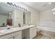 Bright bathroom featuring double sinks, a large mirror with vanity lighting, and a tiled bathtub at 318 Australian Way, Davenport, FL 33897