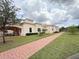 The exterior of a clubhouse featuring a red brick walkway, tan facade, and well-maintained landscaping at 2612 Shantiniketan Blvd # G12, Tavares, FL 32778