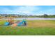 Spacious backyard with a playground, fire pit, and a view of the pond with neighborhood homes in the background at 4432 Seven Canyons Dr, Kissimmee, FL 34746