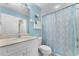 Bright bathroom with a single sink vanity, tile flooring, a toilet, and a tub-shower combo with blue curtain at 5300 S Atlantic Ave # 16-505, New Smyrna Beach, FL 32169