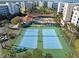 Aerial view of tennis courts and a pool/patio area with palm trees and residential buildings in the background at 5300 S Atlantic Ave # 16-505, New Smyrna Beach, FL 32169