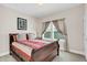 A bedroom featuring a wooden bed frame, large window with blinds and curtains, and neutral carpeting at 1545 Caterpillar St, St Cloud, FL 34771