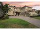 Beautiful two-story home with a three-car garage, brick driveway, and vibrant landscaping under a stunning colorful sunset sky at 1082 Trappers Trail Loop, Davenport, FL 33896