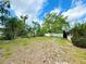 A grassy backyard with shade trees and a partial white picket fence under a partly cloudy sky at 1931 N Portillo Dr, Deltona, FL 32738
