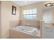 Large soaking tub in bathroom featuring neutral tile, a picture window, and white cabinets at 426 Vista Loop, Davenport, FL 33897