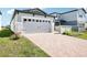 A wide gray two-car garage is featured with stone accents and a brick driveway at 667 Pennywort St, Lake Alfred, FL 33850