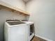 Well-lit laundry room featuring a modern white washer and dryer set, complemented by a rustic wooden shelf at 2241 Mystic Maze Ln, Minneola, FL 34715