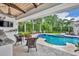 A backyard patio with outdoor kitchen, television, wicker furniture, and a beautiful blue swimming pool at 940 Lincoln Cir, Winter Park, FL 32789