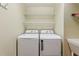 A laundry room with a white washer and dryer and some metal shelving above the appliances at 3198 Abana Path, The Villages, FL 32163