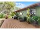 Deck with BBQ grill, lounge chair, and potted plants attached to a green house with lush surrounding landscaping at 1200 Auger Dr, New Smyrna Beach, FL 32168