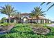 Well-maintained community entrance with stucco walls, a tile roof, and vibrant landscaping at 7224 Oakmoss Loop, Davenport, FL 33837