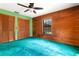 Bedroom with wood walls, ceiling fan, plush turquoise carpet, and windows for natural light at 5180 Garlanger Trl, Oviedo, FL 32765