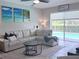 Bright living room featuring a white sectional sofa, coastal art, and views of the pool through a large window at 14400 Saint Georges Hill Dr, Orlando, FL 32828