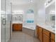 Bright bathroom featuring a glass enclosed shower, tub under arched window, and double wooden vanity at 2853 Strand Cir, Oviedo, FL 32765