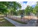 Outdoor tennis court enclosed with a chain-link fence and surrounded by mature trees near a sidewalk at 718 Wildwood Dr, Winter Springs, FL 32708
