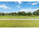 Image shows a large vacant lot with green grass and trees under a blue sky with white clouds at 2640 Shelby Ruth Pl, St Cloud, FL 34769