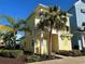 Inviting two-story yellow home with a cute balcony, lush greenery, and a yellow chair on the porch at 3013 Latitude Ln, Kissimmee, FL 34747