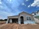 Single-Gathering home featuring gray stucco, an attached garage, and a covered entryway under a sunny blue sky at 5250 Teirgarten St, St Cloud, FL 34771