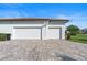 White three-car garage with a brick driveway, with green grass, bushes, and a clear blue sky at 11706 Waterstone Loop Dr, Windermere, FL 34786