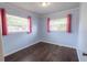 This bedroom features wood-look floors, two windows with red curtains and neutral paint at 3300 Needles Dr, Orlando, FL 32810