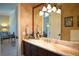Bathroom vanity features a long marble countertop, dark cabinets, and a large mirror with decorative light fixture at 11013 Ullswater Ln, Windermere, FL 34786