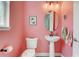 Stylish half bathroom featuring pink walls, a pedestal sink, and a modern, oval mirror at 15378 Gilligan Ct, Winter Garden, FL 34787