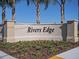 Rivers Edge community entrance sign surrounded by mulched garden, tall trees, and blue sky at 2710 Golden Trout Ln, Edgewater, FL 32141