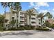Inviting condo building with multiple balconies, palm trees, lush landscaping, and ample parking for residents and guests at 7660 Whisper Way # 402, Reunion, FL 34747