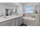 Bright bathroom featuring double sinks, quartz counters, and a soaking tub with a view at 1123 Dora Parc Ln, Mount Dora, FL 32757