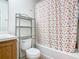 Bathroom with wood vanity, shelving unit, toilet, and bathtub/shower with colorful flower shower curtain at 2662 Mayaguana St, Kissimmee, FL 34747