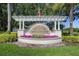 Community entrance sign for 'Enclave at Berkshire Park', featuring flowers, mature trees, and a U.S. flag at 7201 Halton Ct, Windermere, FL 34786